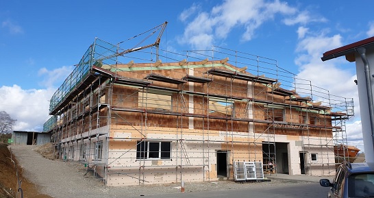 Am neuen Standort der HFH Präzisionsmechanik GmbH entsteht ein Firmengebäude im Neubau, eingerüstet und teilweise verputzt unter blauem Himmel.