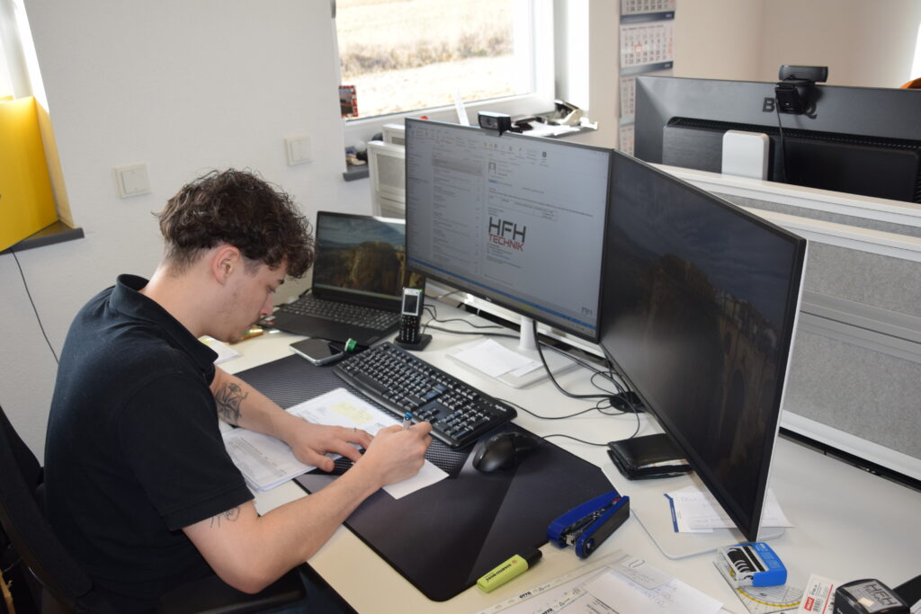 Ein Mitarbeiter arbeitet am CAD-Arbeitsplatz mit mehreren Monitoren und prüft technische Unterlagen bei HFH Präzisionsmechanik in Niederbayern.