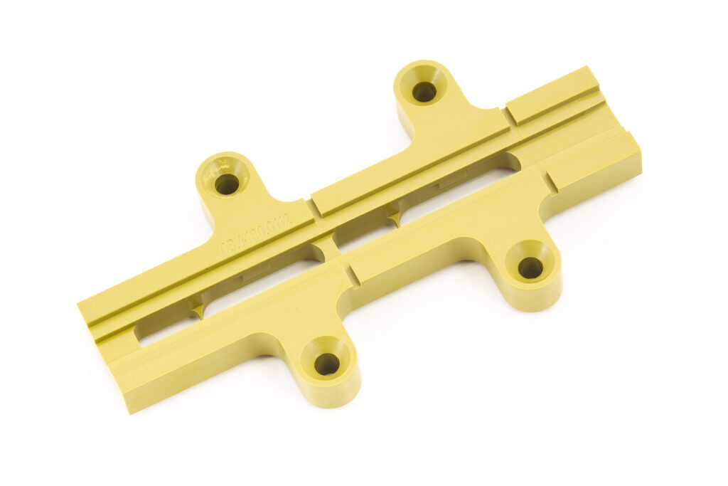 Bei HFH Präzisionsmechanik GmbH zeigt ein gelbes CNC-Frästeil aus Kunststoff präzise Bohrungen, Nuten und saubere Konturen für die Fertigung in Bayern.