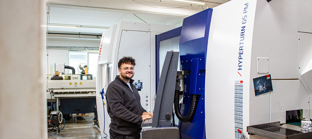 Im Werk steht ein CNC-Dreh-Fräszentrum Hyperturn 65 PM, an dem ein Mitarbeiter präzise Dreh-Fräsarbeiten für komplexe Bauteile vorbereitet.