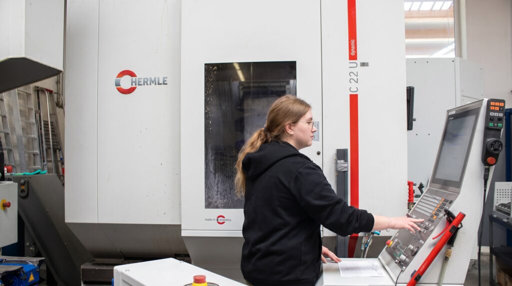 Eine Mitarbeiterin bedient an einer Hermle C 22 dynamic die CNC-Steuerung in der Werkhalle von HFH Präzisionsmechanik GmbH.