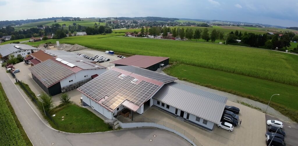 Über dem Firmenstandort von HFH Präzisionsmechanik in Niederbayern liegen Hallen mit Solardächern neben grünen Feldern und Zufahrten.